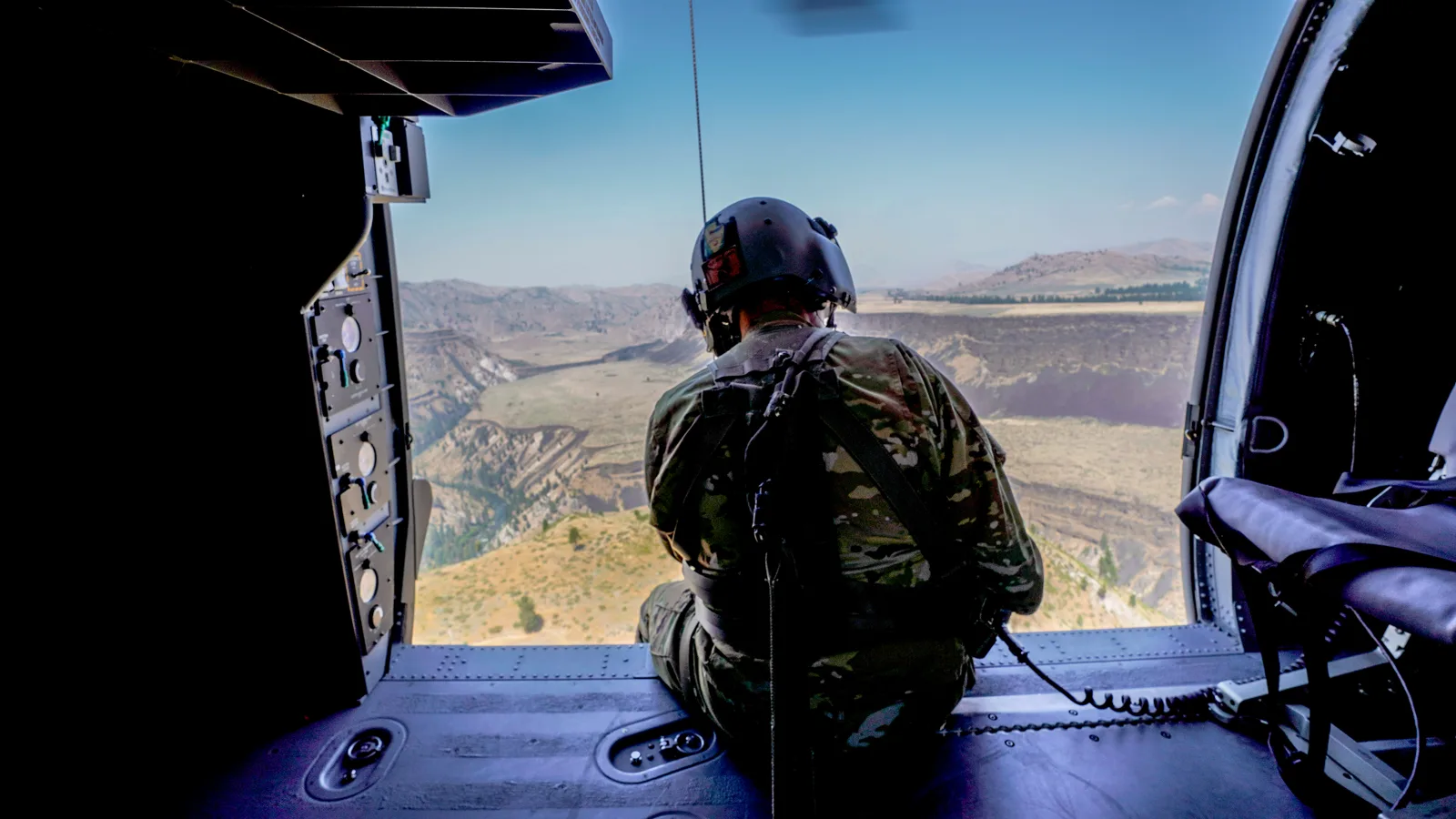 Idaho Army National Guard crew chief sits in the open door of a Black Hawk over Idaho ridgelines, photo by Rusty Rehl