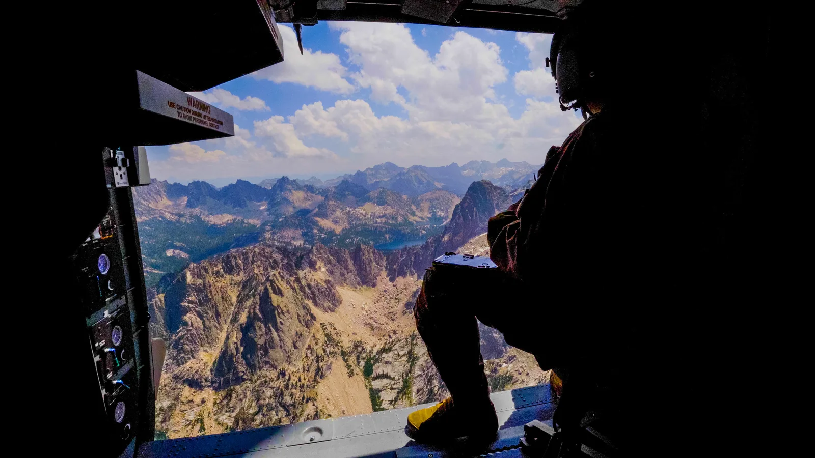 Crew member silhouetted in a Black Hawk door above Idaho's Sawtooth Mountains, photo by Rusty Rehl
