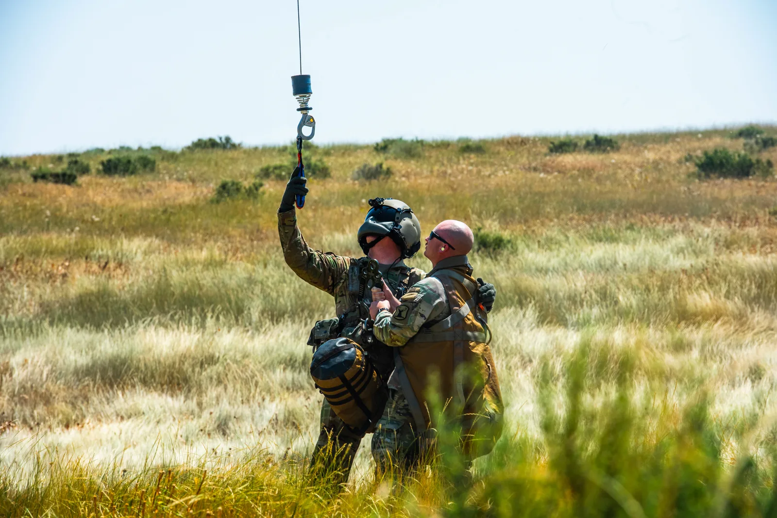Idaho Army National Guard soldiers guide a helicopter hoist cable in a grass field, photo by Rusty Rehl