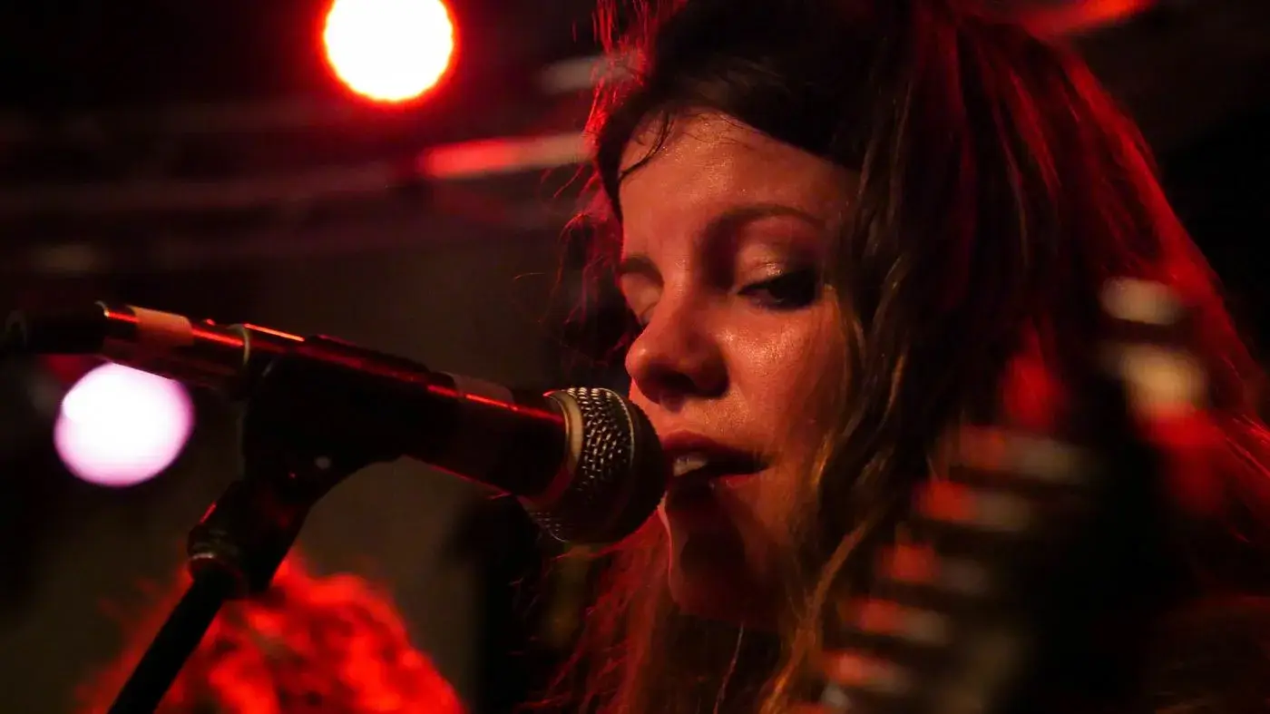 Singer at the microphone under red stage light in Boise, Idaho, concert photo by Rusty Rehl