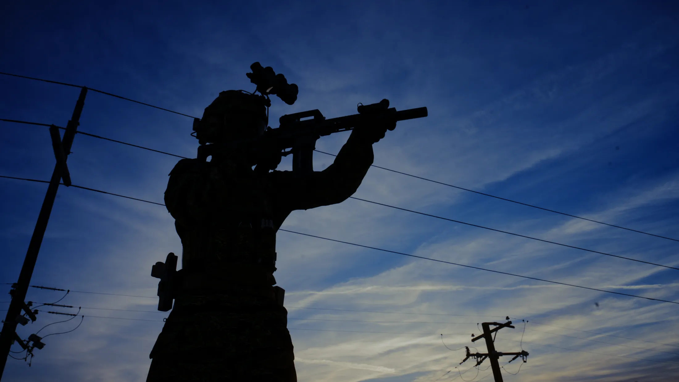 Commando silhouette with night-vision goggles aiming a rifle against a deep blue dusk sky and power lines, Rusty Rehl's ad for Combat Sport Supply