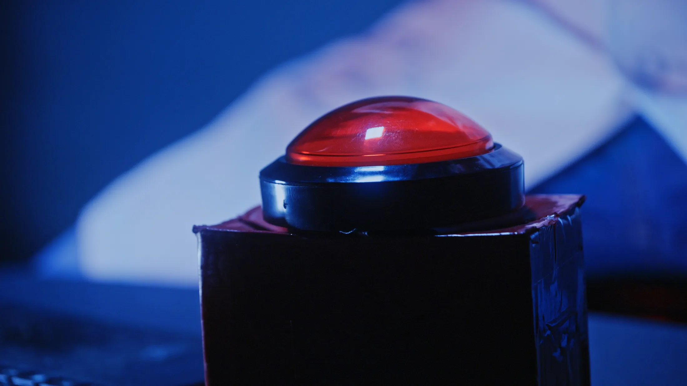 Close-up of a large red button in cool blue light with a white lab coat blurred behind it, still from Rusty Rehl's ad for Combat Sport Supply