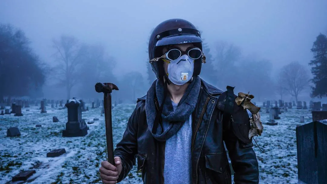 Figure in a helmet, goggles and dust mask holding a hammer in a foggy cemetery, cinematic portrait by Rusty Rehl