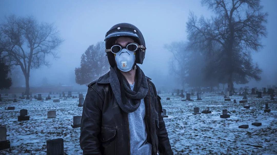 Figure in a helmet, goggles and dust mask standing in a foggy, snow-dusted cemetery, cinematic portrait by Rusty Rehl