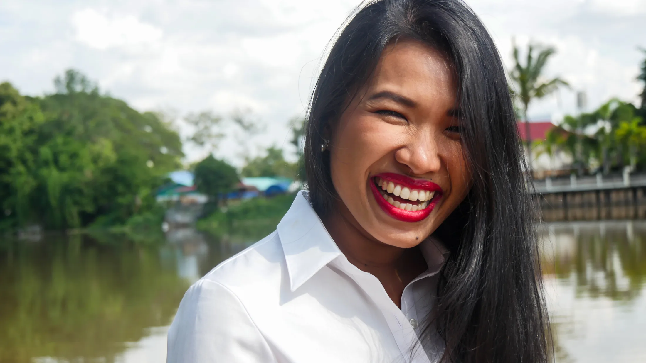 Woman in a white shirt and red lipstick laughing by a river in Thailand, portrait by Boise, Idaho photographer Rusty Rehl