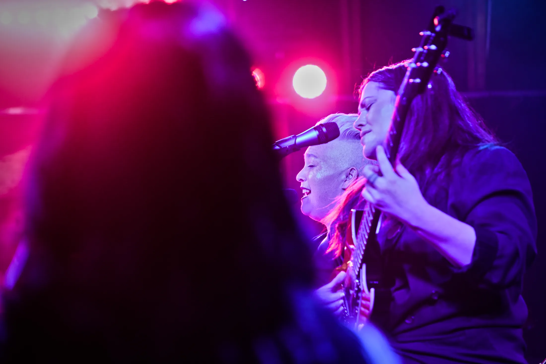 Singer and guitarist sharing a microphone in red backlight, Boise, Idaho concert photo by Rusty Rehl