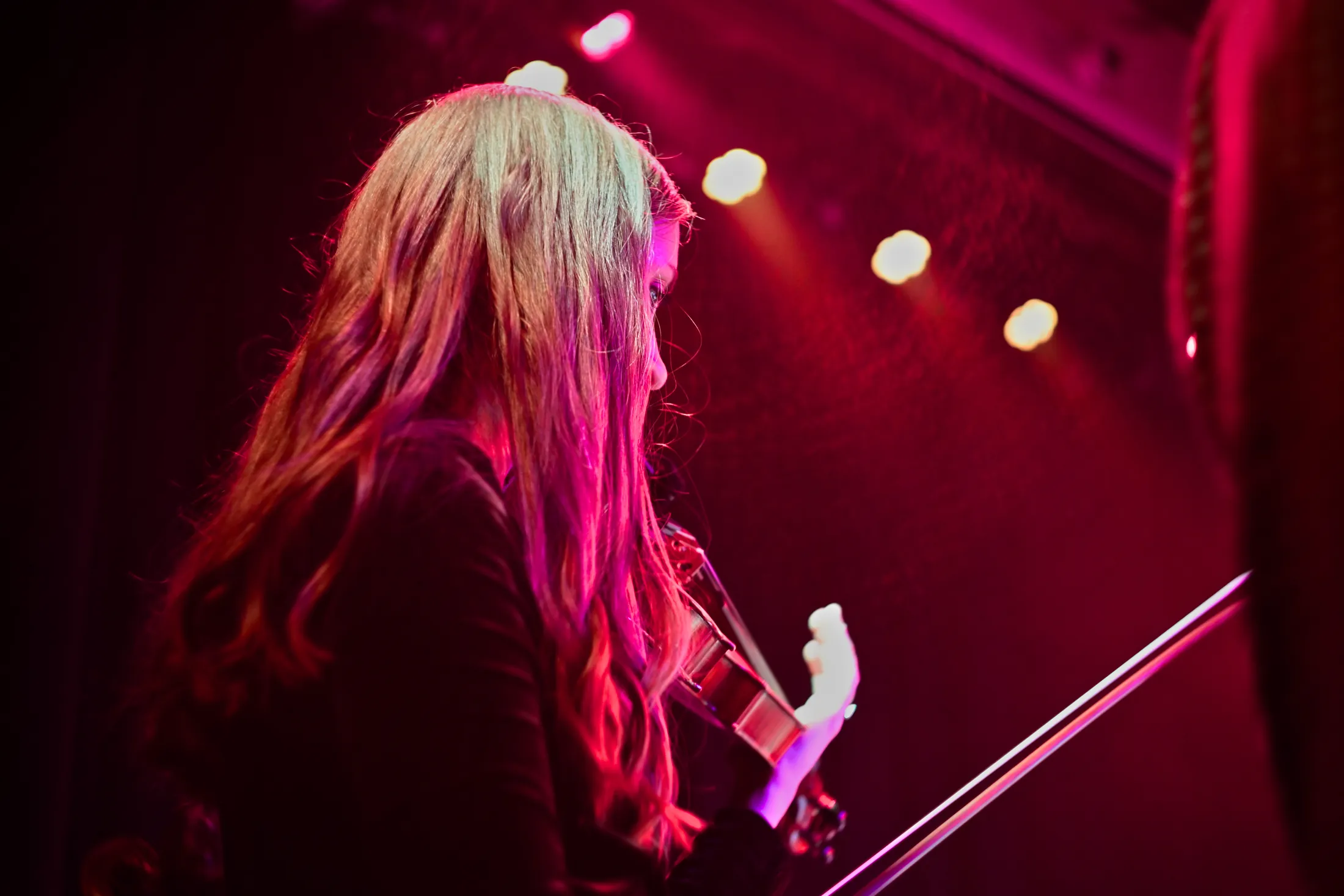 Long-haired violinist in red light with stage lights behind, Boise, Idaho concert photo by Rusty Rehl