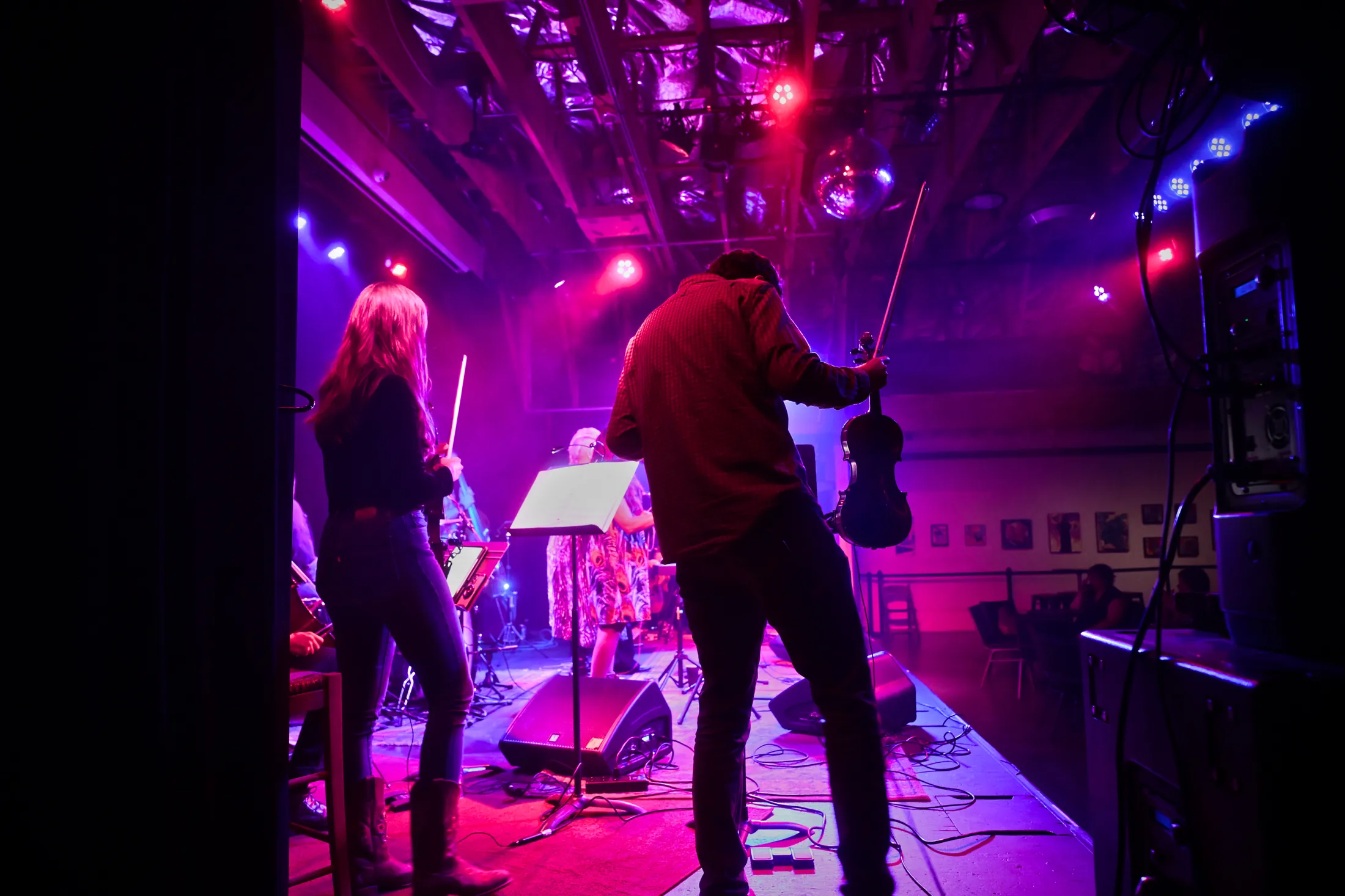 Two violinists at the side of a red-lit stage, Boise, Idaho concert photo by Rusty Rehl