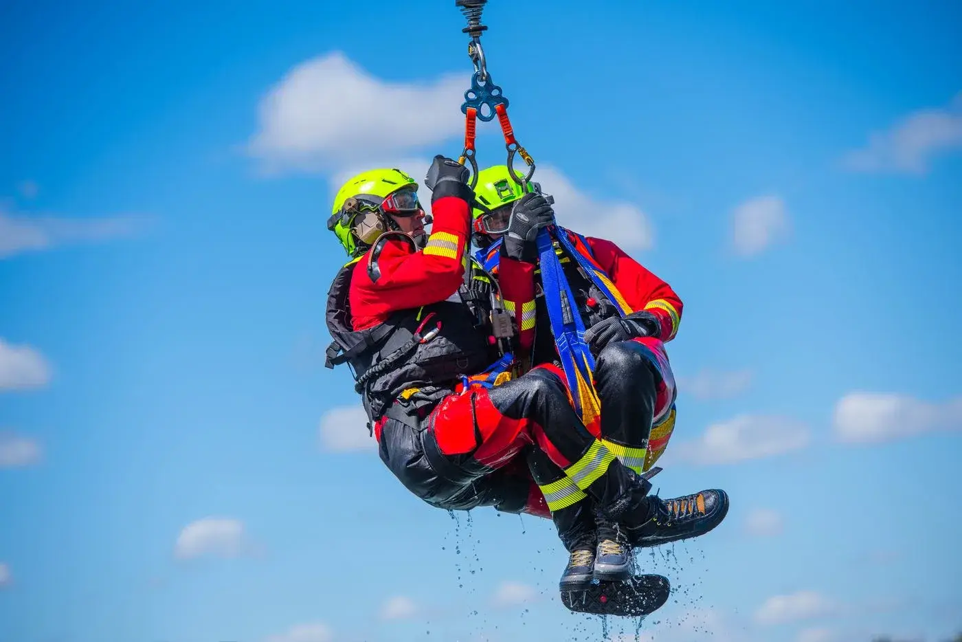 Two rescuers in red dry suits ride a helicopter hoist during Idaho National Guard rescue training, photo by Rusty Rehl