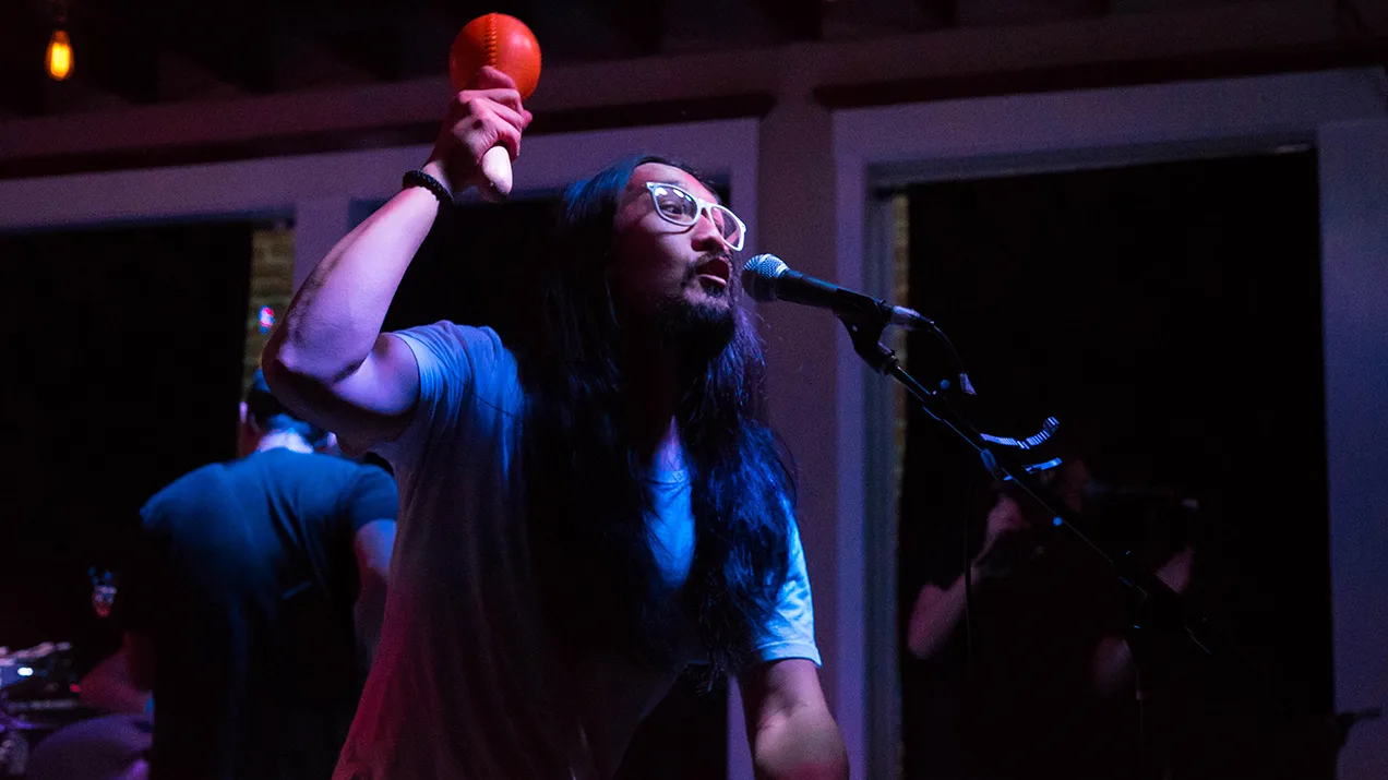 Run River North singer raising a maraca at the microphone in blue light, concert photo by Rusty Rehl